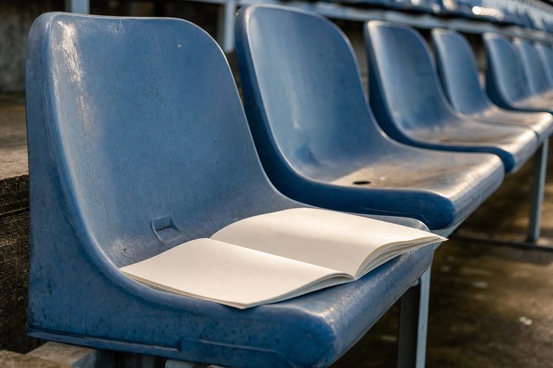Un fascicolo aperto su un seggiolino di una tribuna vuota – immagine generata con AI.